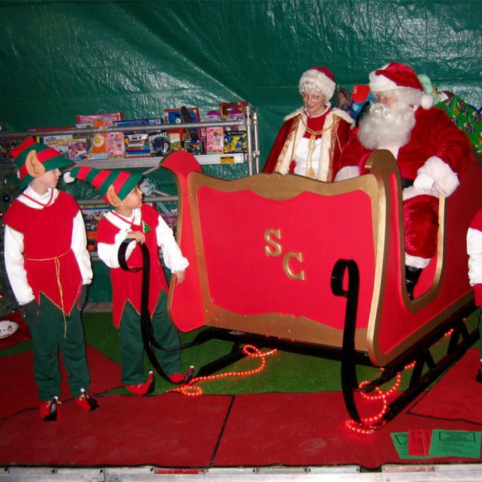 Santa and Mrs. Claus in sleigh with two kid elves